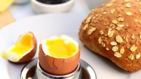 Ein weichgekochtes Frühstücksei steht in einem Eierbecher, die gelbe Füllung ist sichtbar. Daneben liegt ein Brötchen.