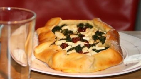 Ein Pide mit Spinat und Schafskäse liegt auf einem Teller, umgeben von einem Glas, auf einem rustikalen Tisch.