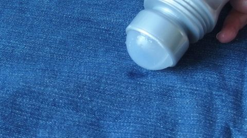 Ein Deoroller wird auf einen blauen Stoff gedrückt, um einen Fleck auf der Kleidung zu entfernen.