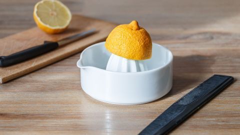 Eine Zitronenpresse mit einer ganzen Zitrone im Inneren steht auf einem Holztisch, um frischen Zitronensaft zu gewinnen.