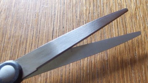 Eine Schere schneidet präzise auf einer Holzoberfläche, ideal zum Scheren von Kleberesten.