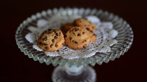 Auf einem eleganten Glasstil steht ein Teller mit knusprigen Mandel-Cookies, die mit Schokostückchen verziert sind.