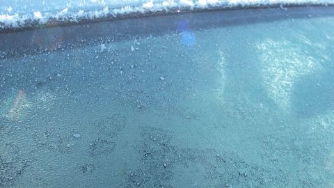 Mit diesem Trick vereist das Tiefkühlfach nicht wieder so schnell: Das Fach einfach mit Alufolie auslegen. Auf einer Autoscheibe ist Eis zu sehen, während eine Schicht Alufolie außen angebracht ist, um das Vereisen zu verhindern.
