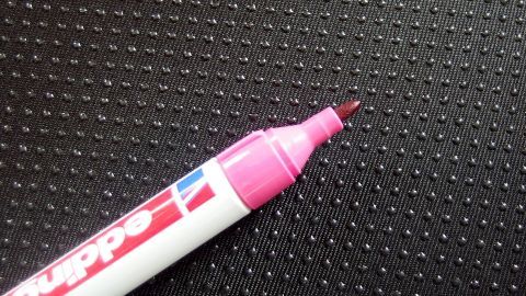 Ein Edding-Marker liegt auf einer strukturierten, glatten Oberfläche. Der Marker ist pink und bereit zu schreiben.