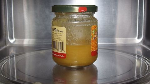 Wie wird kristallisierter Honig wieder flüssig? Ganz einfach in der Mikrowelle. Ein Glas kristallisierter Honig steht in einer Mikrowelle und wird erwärmt, um wieder flüssig zu werden.