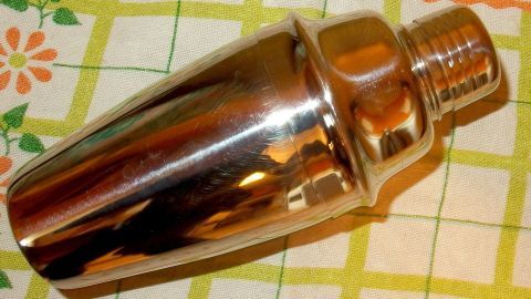 Dieser Tipp stellt eine Methode vor, wie man einen klemmenden Cocktailshaker wieder auseinander bekommt. Ein Cocktailshaker liegt auf einem karierten Küchentuch und scheint klemmen zu wollen, während er glänzt.