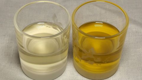 Zwei Gläser mit verschiedenen Ölen, eines klar und eines goldfarben, stehen nebeneinander auf einem hellen Tuch.