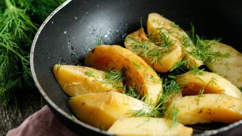 Gekochte Kartoffeln liegen in einer Pfanne, garniert mit frischem Dill, umgeben von einer grünen Dillpflanze.