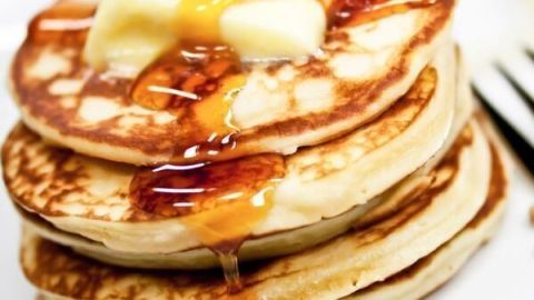 Stapel von American Pancakes, übergossen mit Sirup und einer Butterflocke, serviert auf einem weißen Teller.