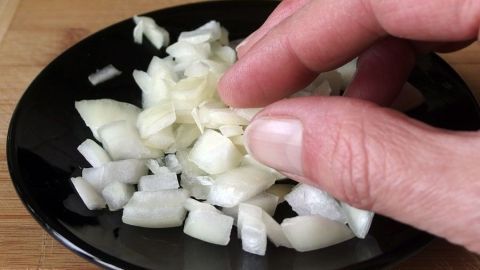 Eine Hand greift nach gehackten Zwiebeln auf einem schwarzen Teller, verursacht stinkende Finger und zeigt Zubereitungsprozess.