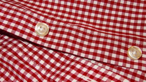 Wer nicht gerne Knöpfe annäht, der kann sich die Arbeit mithilfe von farblosem Nagellack sparen. Zwei farblose Knöpfe auf einem rot-weiß karierten Hemd fixieren die Stofflagen, um ein einheitliches Design zu schaffen.