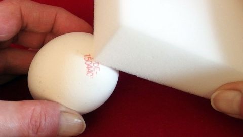 Ein weißes Ei wird mit einem Schmutzradierer bearbeitet, um einen roten Stempel zu entfernen. Der Hintergrund ist rot.