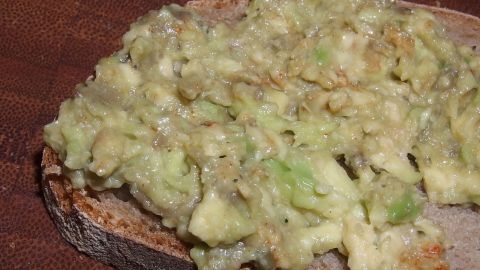 Guacamole bedeckt ein Stück Brot auf einem rustikalen Holzbrett; cremige Textur zeigt frische Zutaten.