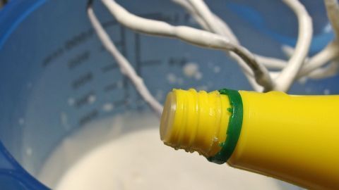Eine Flasche Zitronensaft wird über einer Schüssel mit Sahne gehalten, während der Mixer zur Zubereitung bereitsteht.