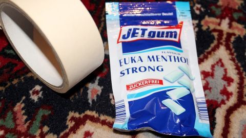 Ein Beutel mit Kaugummi und ein Klebeband liegen auf einem bunten Teppich, was eine alltägliche Umgebung schafft.