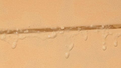 Wassertropfen stehen an einer Silikonfuge zwischen Fliesen, die möglicherweise Schimmelansätze zeigen.