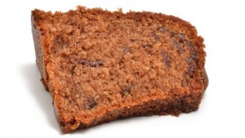 Ein Stück Rotweinkuchen liegt auf einer weißen Oberfläche, mit feuchter, krümeliger Textur und dunklen Schokoladenflecken.