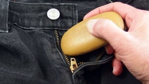 Bei klemmendem Reißverschluss hilft es, einmal mit einem Stück Seife darüber zu reiben. Eine Hand hält ein Stück Seife, das in einen klemmenden Reißverschluss einer Jeans gedrückt wird, um ihn zu lösen.