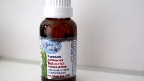Sekundenkleber auf der Haut ist besonders unangenehm: Wie bekommt man ihn wieder entfernt? Nimm verdünntes Teebaumöl! Ein braunes Fläschchen mit Teebaumöl steht auf einem Tisch, bereit zum Einsatz, um Superkleber von Händen zu entfernen.