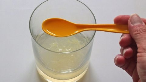 Ein Hand mit einem gelben Löffel rührt in einem Glas mit Flüssigkeit, um eine Erkältung zu lindern.