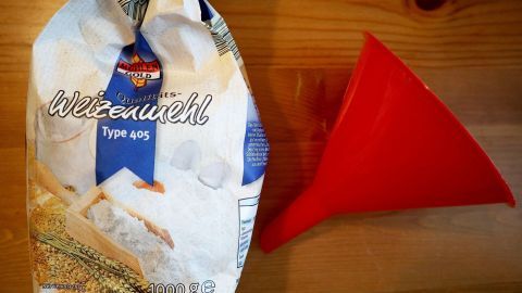 Mithilfe eines Trichters lässt sich das Verklumpen einer Soße verhindern. Ein roter Trichter steht neben einer Tüte Weizenmehl, um Soßenklumpen beim Einfüllen zu verhindern.