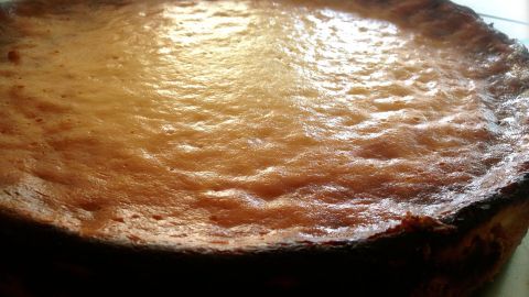 Ein Käsekuchen liegt auf einem Tisch, glänzend und goldgelb, bereit zum Servieren in einer heimeligen Küche.