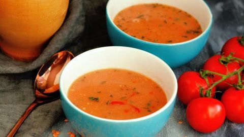 In zwei Schalen dampft die cremige Linsensuppe, umgeben von frischen Tomaten und Sesam für eine rustikale Präsentation.
