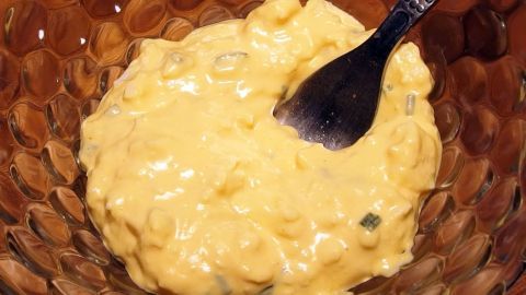 Ein gelber Eiersalat wird mit einem Löffel in einer transparenten Schüssel angerührt und sieht cremig aus.