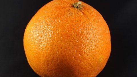 Eine leuchtend orangefarbene Orange liegt auf einem schwarzen Hintergrund, bereit, frisch gepresst oder verzehrt zu werden.