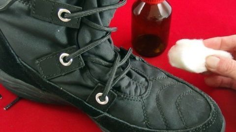 Ein schwarzer Schuh wird mit einer Wattebällchen getränkt in Alkohol behandelt, um ihn zu weiten. Im Hintergrund steht eine Flasche.