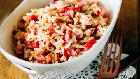 Ein Reissalat in einer weißen Schüssel wird serviert, umgeben von einem Spitzenuntersetzer und Besteck.