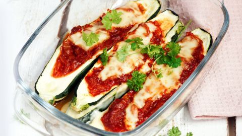 Zucchinihälften sind mit Tomatensauce und Käse gefüllt, garniert mit frischem Koriander in einer Glasform.