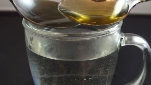 Heißes Wasser mit Honig und Apfelessig gegen Erkältung. Ein Glas heißes Wasser enthält zwei Löffel, einer mit Honig, bereit zur Einnahme gegen Erkältungssymptome.