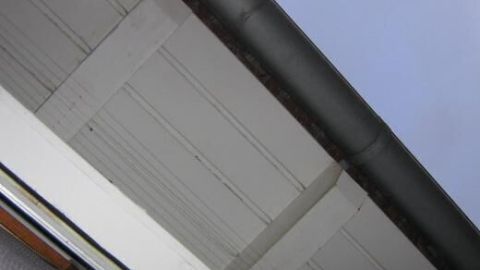 Dachuntersicht mit dunkler Dachrinne, sichtbar von unten, zeigt klare Linien unter blauem Himmel.