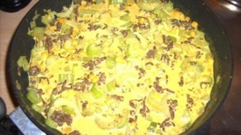 Eine Pfanne mit asiatischer Curry-Hack-Mischung kocht auf dem Herd; Stücke von Staudensellerie und Mais sind gut sichtbar.