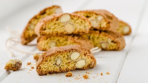 Cantuccini liegen gestapelt auf einer weißen Oberfläche, während sie in Stücke geschnitten sind und Mandeln sichtbar sind.
