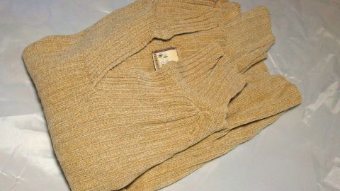 Ein beiger Pullover liegt ordentlich gefaltet auf einer hellen Oberfläche, bereit für den Verkauf von Secondhand-Klamotten.
