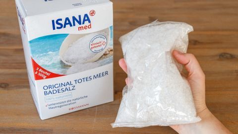 Eine Hand hält eine Tüte mit Himalaya-Salz, daneben steht eine Packung mit ISANA Badesalz zur Schwellungslinderung.