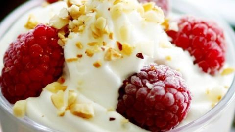 Eine cremige Himbeer-Sahne-Creme wird in einem Glas serviert, garniert mit frischen Himbeeren und gehackten Nüssen.