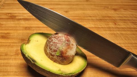 Ein Messer schneidet in eine Avocado, um den kern auszunehmen, auf einer Holzarbeitsfläche.