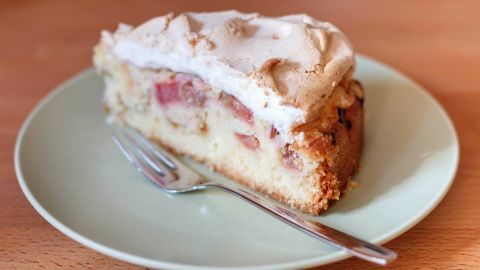 Ein Stück Obstkuchen liegt auf einem grünen Teller, mit einer Gabel daneben, auf einer Holzoberfläche.