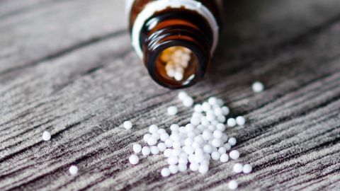Pulsatilla D 12 hilft super bei starken Regelschmerzen. Ein homöopathische Mittel, in Form von Kügelchen. Kleine homöopathische Kügelchen aus einer geöffneten Flasche liegen auf einem Holzuntergrund und können gegen Regelschmerzen helfen.