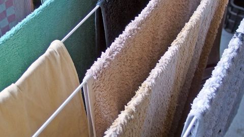 Bunte Handtücher hängen auf einer Wäscheleine und trocknen im Innenraum, weich und frisch gewaschen ohne Weichspüler.