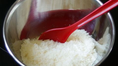 Arbeitsersparnis beim Hobeln von Parmesan - Parmesan hobeln für Faule. Eine Schüssel mit geriebenem Parmesan, während ein roter Löffel den Käse sanft umrührt – ein einfaches Rezeptkontext.