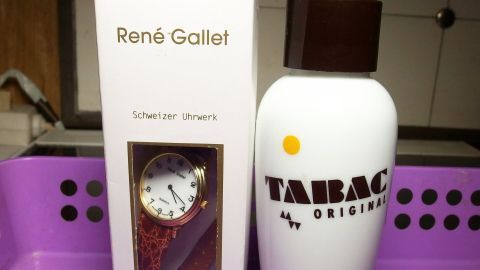 Ein Geschenkkarton zeigt eine Uhrenverpackung von René Gallet neben einem Tabac Original Flakon in einer lila Box.