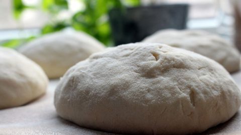 Der Hefeteig liegt formbar auf einer Holzunterlage, während im Hintergrund Pflanzen die Küche beleben, bereit zum Backen.