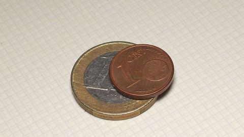 Zwei Euro-Münzen liegen auf einer hellen Oberfläche, was die Frage aufwirft, ob Geld für den Einkaufswagen nötig ist.