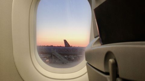 Ein Flugzeugfenster zeigt den Abendhimmel und eine landende Maschine von airberlin, während Passagiere in Reihe sitzen.