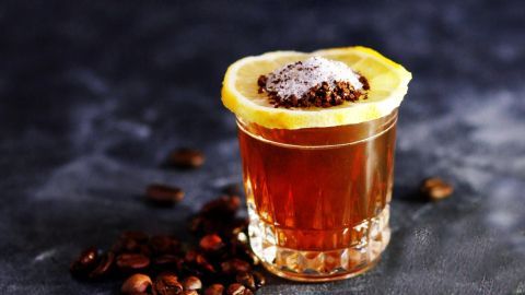 Ein Glas mit einem Getränk aus Koffein und Alkohol, garniert mit einer Zitronenscheibe, steht auf einem dunklen Hintergrund.