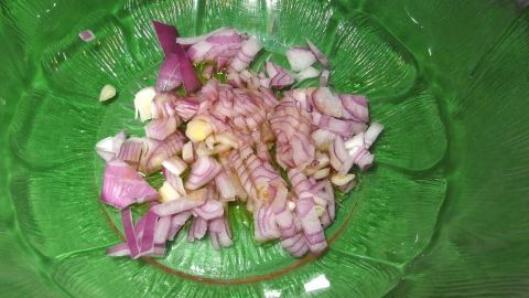 Eine in Öl zerdrückte und verrührte Zwiebel sorgt für eine würzigere Salatsoße. Erst danach werden die restlichen Zutaten der Soße untergerührt. In einer grünen Schüssel liegen fein gehackte Zwiebeln, bereit für eine würzigere Salatsoße.
